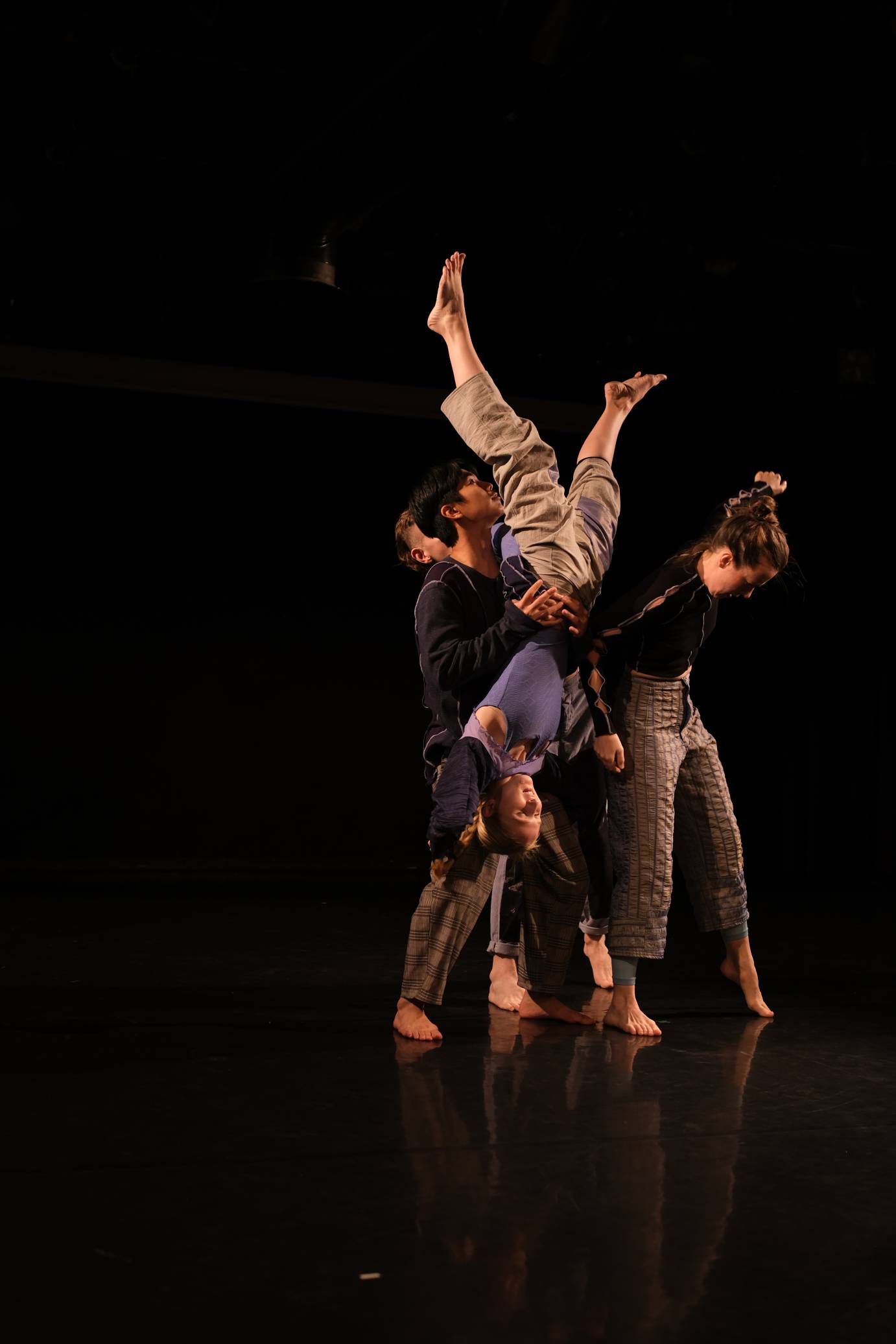 A dancer is held upside down legs askew by three other dancers. 