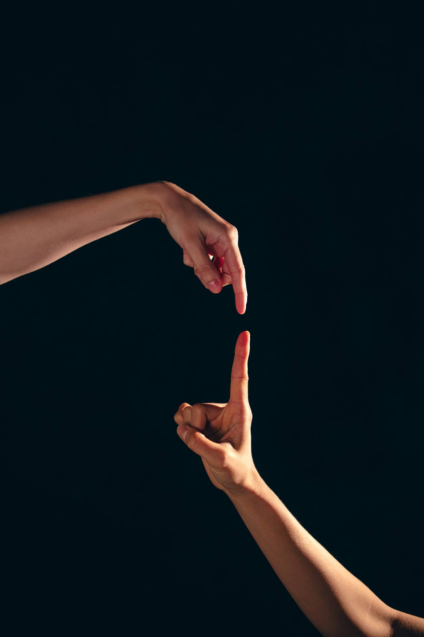 Two hands, one moving downward, the other up, do not touch, but barely.