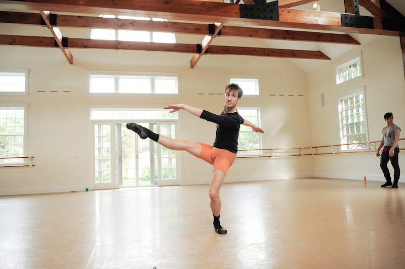 A man in orange shorts extends his leg parallel to the floor.