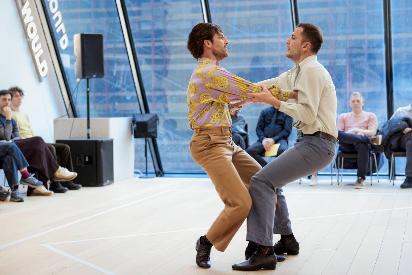 Facing one another, bent arms and knees entwined, the male dancers look into each other's faces and smile.