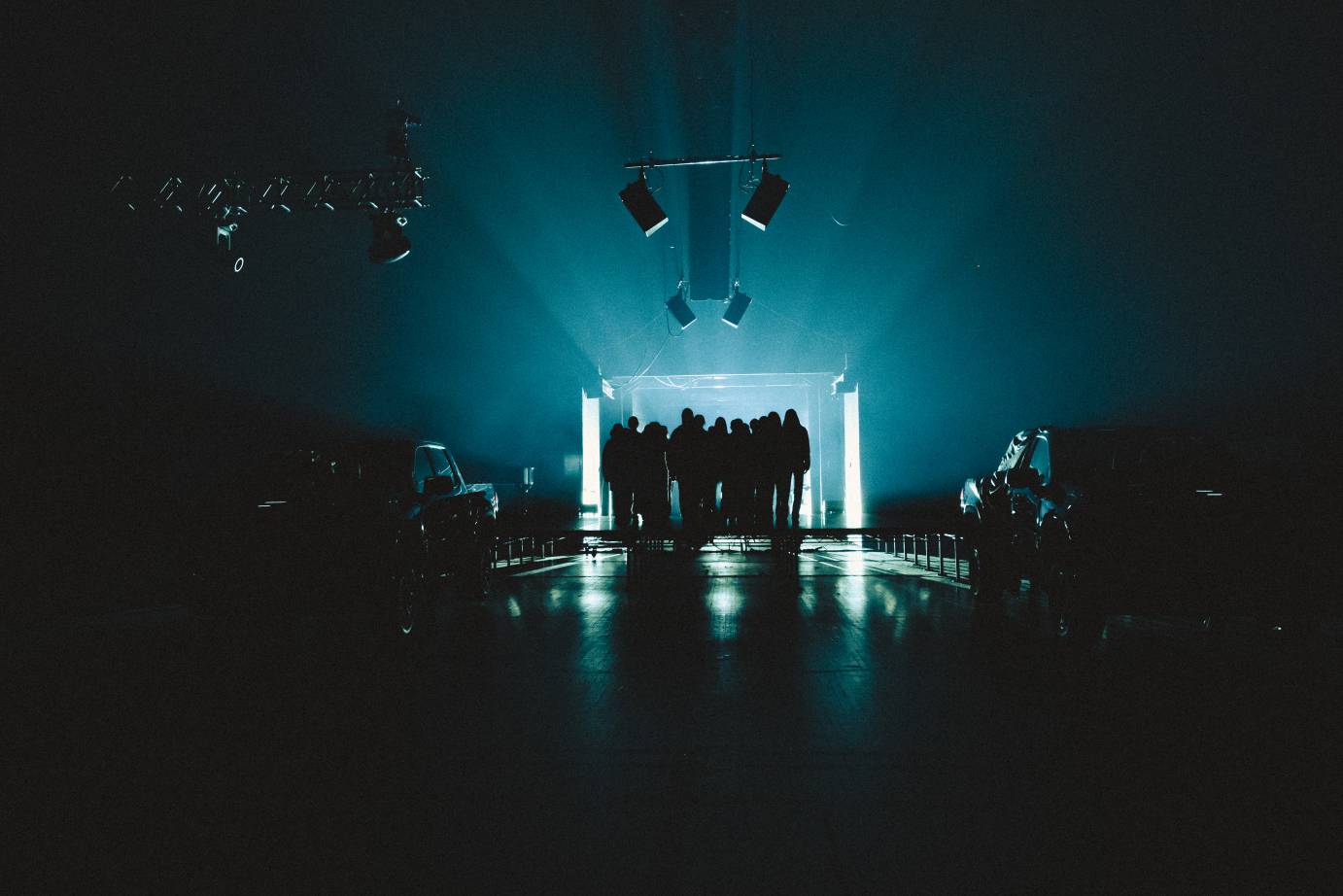 A group of silhouetted performers are back lit as they enter the space.