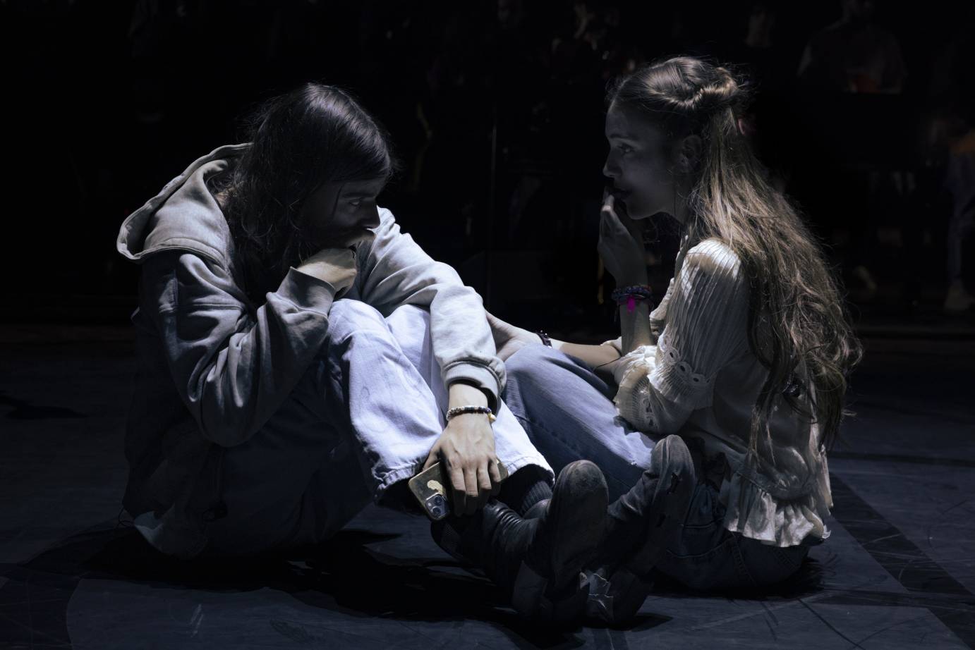 Long-haired Romeo in hoody and Juliet in peasant blouse sit facing one another.