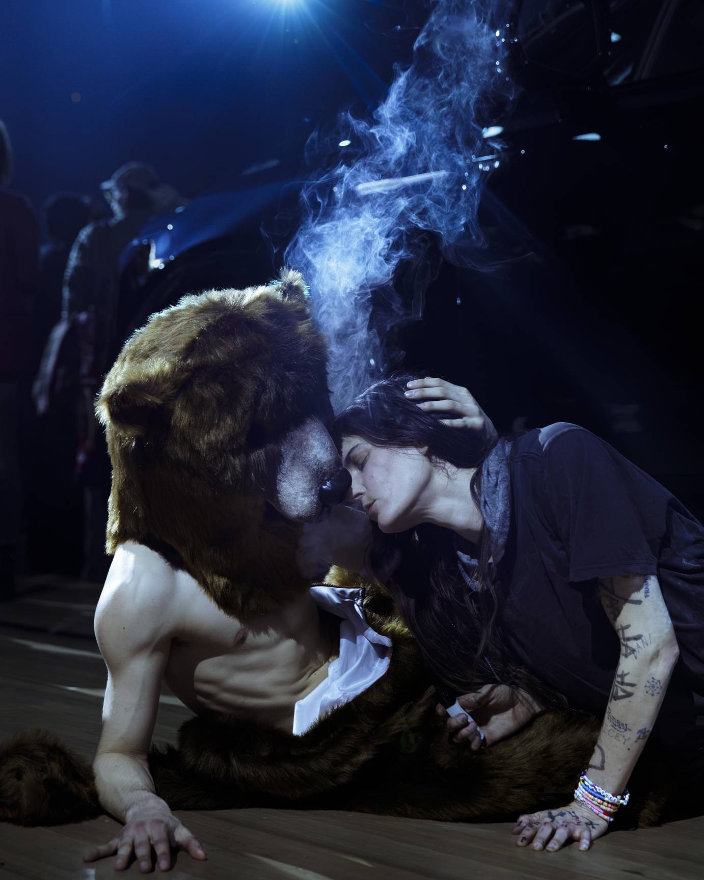 A performer in a bear costume holds the head of a woman close to the bear's face.