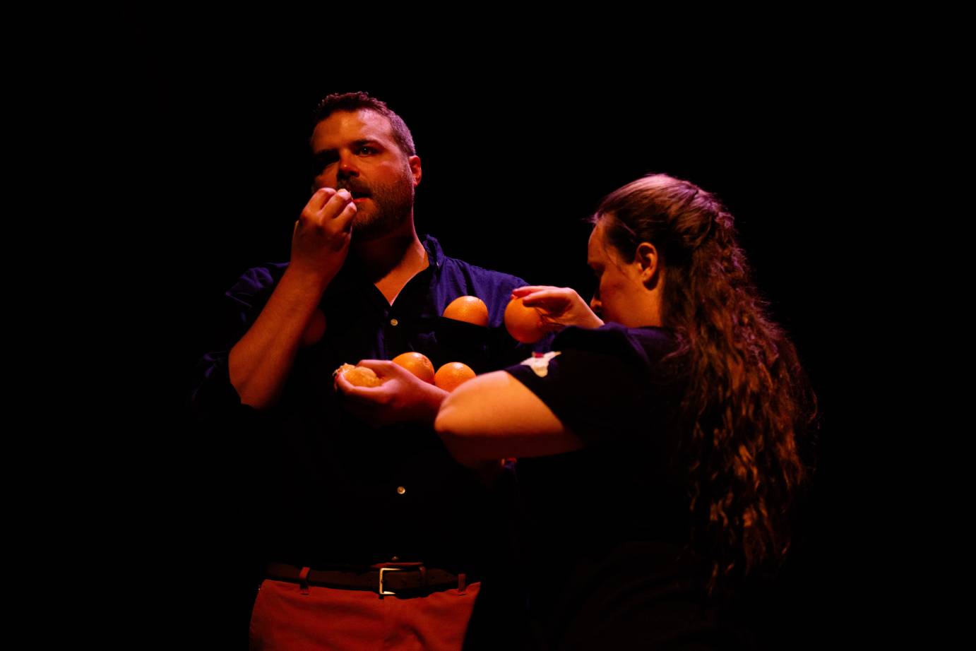 A woman piles oranges into the crook of a bearded man's elbow.