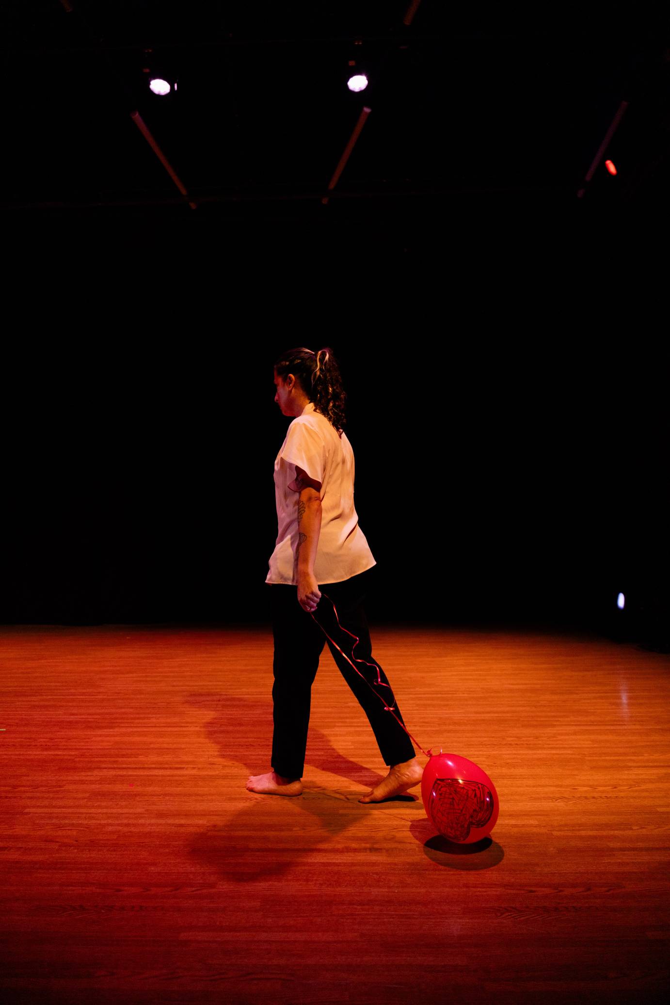 A woman walking upstage trails a red balloon at her feet.