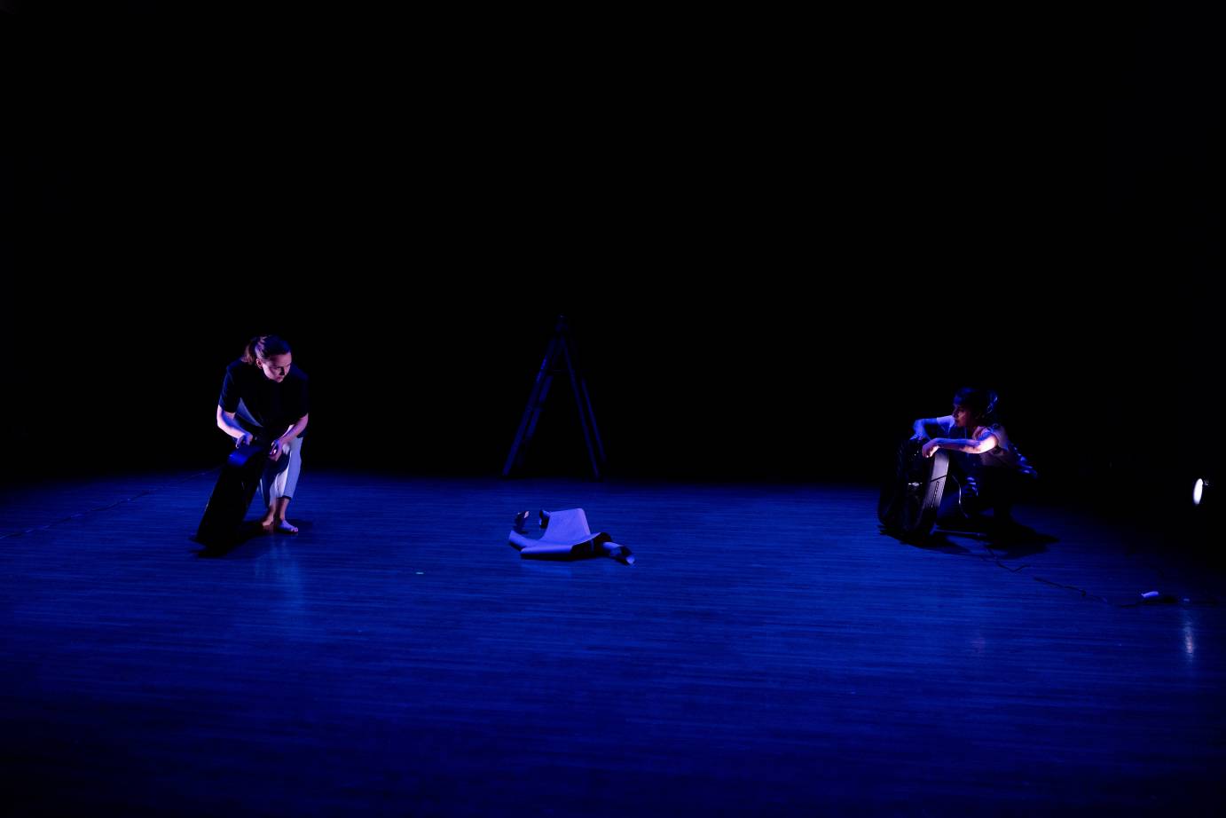 The stage bathed in blue features two performers separated but facing one another. 