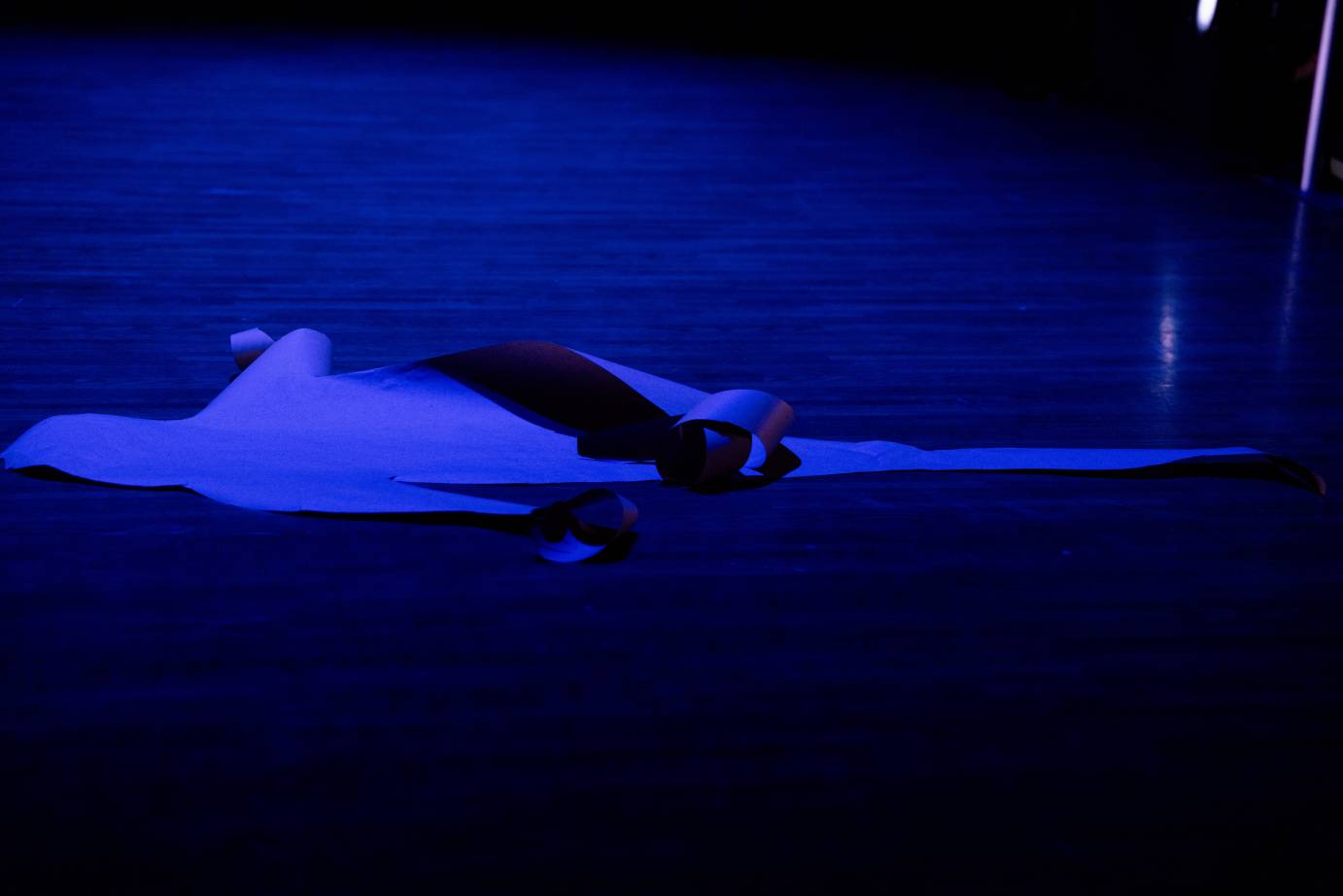 A blue paper cut out of a person lies on the stage bathed in blue light.