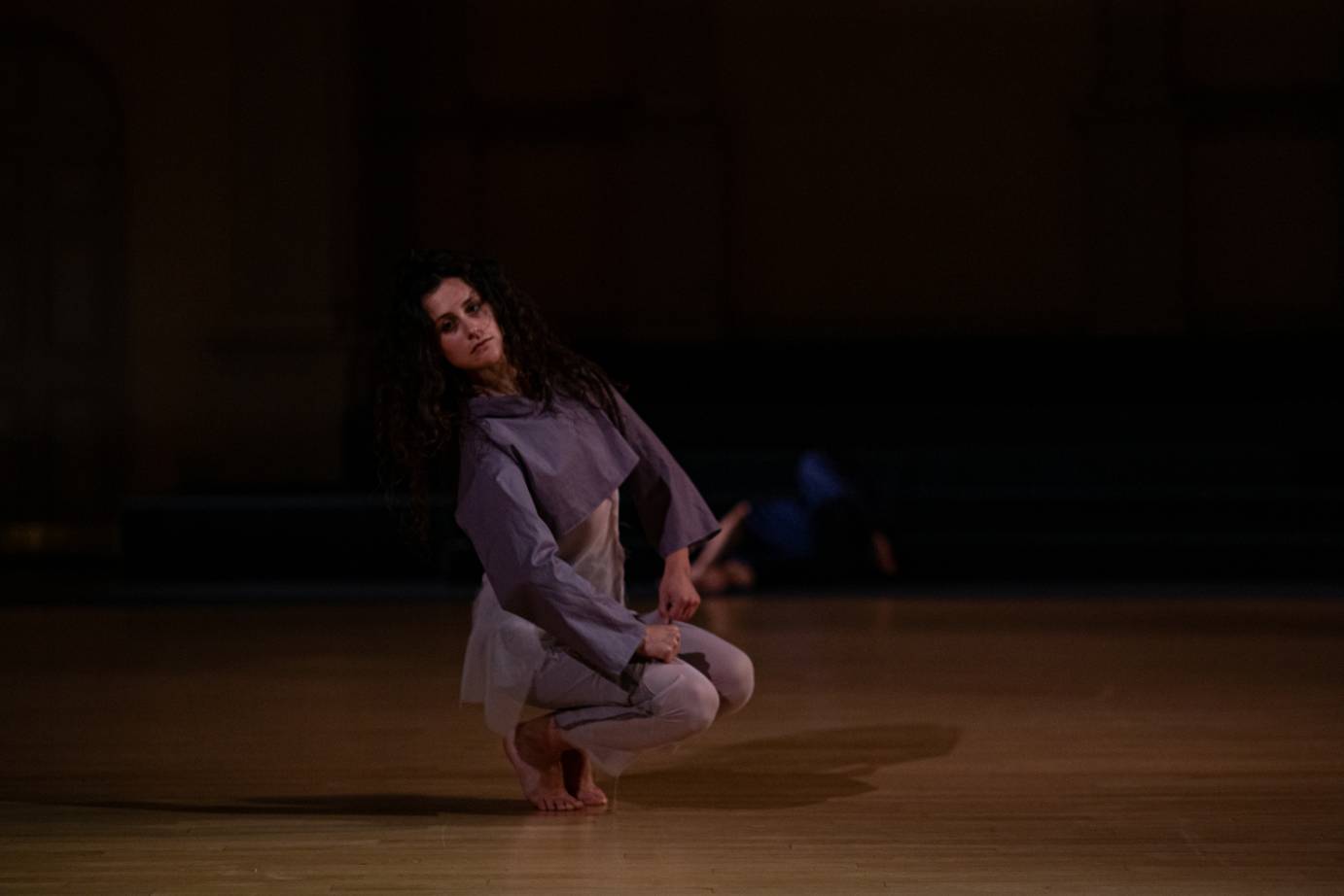 A dark haired woman crouches dressed in a purple costume.