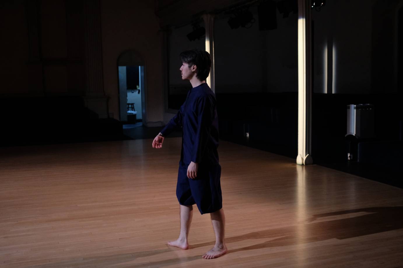A dark haired man in navy blue, stands with the church's column lit in yellow.