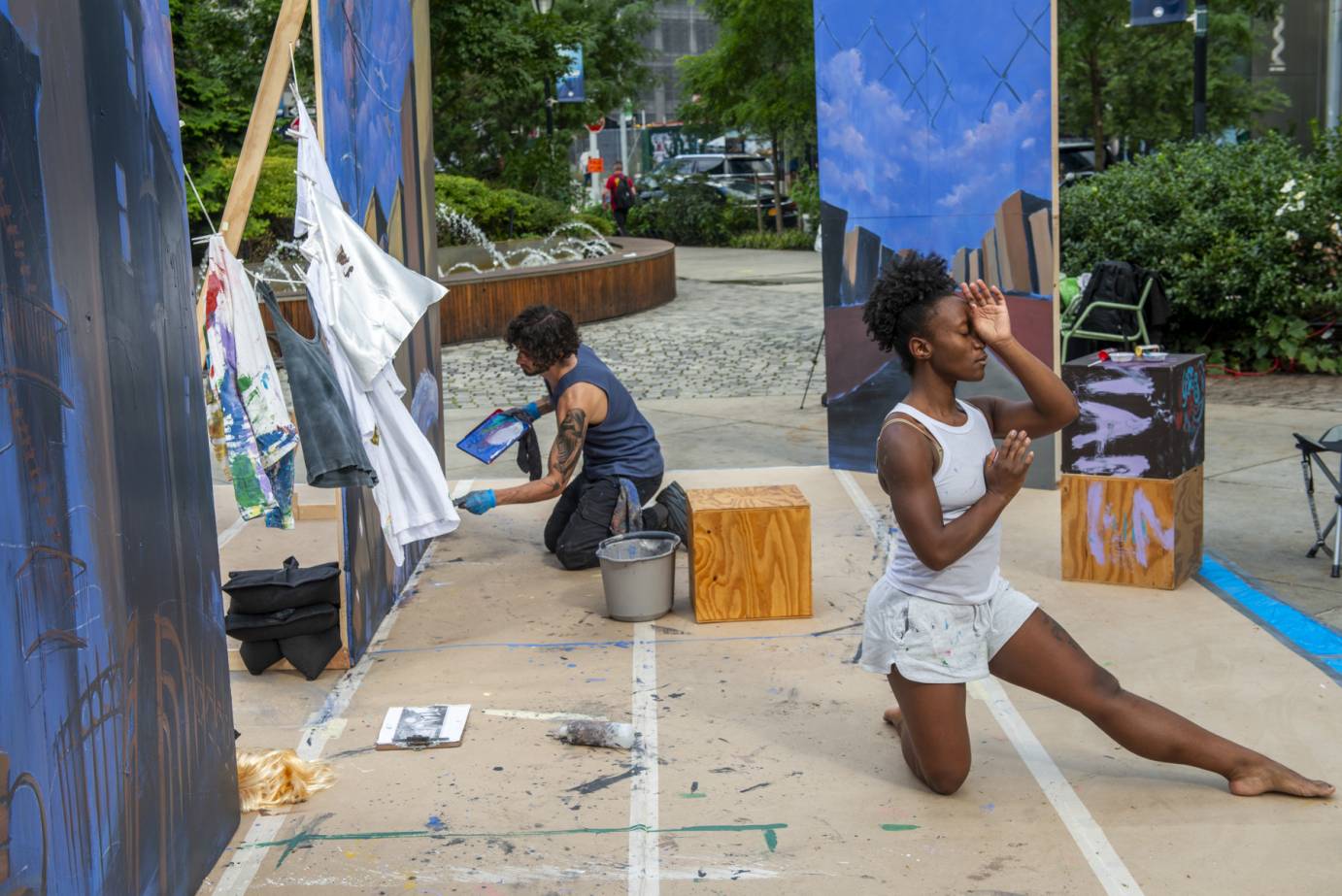 dancer kneels one leg outstretched. man paints on large canvas behind her