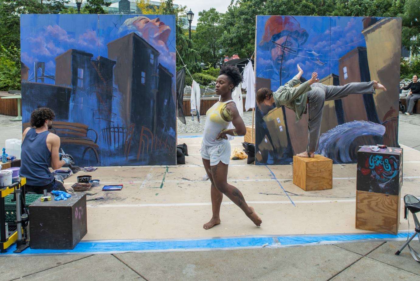 male dancer in pitched arabesque on cube. female standing pose in foreground