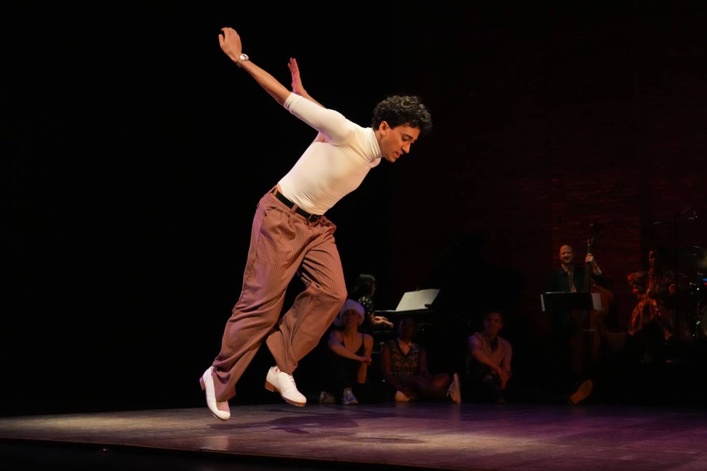 Male dancer both feet off ground in low jump, arms stretched back and body pitched forward