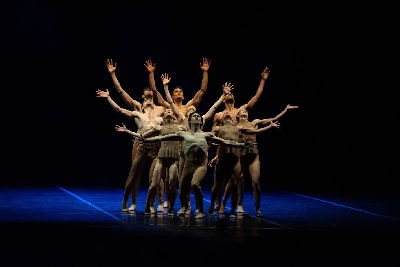 Dancers in a clump, fingers spread and arms uplifted looking like spokes of a wheel