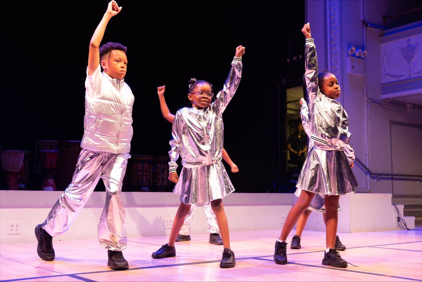 3 children dressed in silver costumes with fists raised upwards