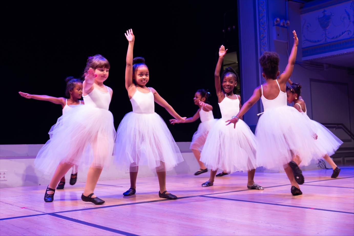 seven child dancers dressed in long white tulle ballet skirts and white leotards