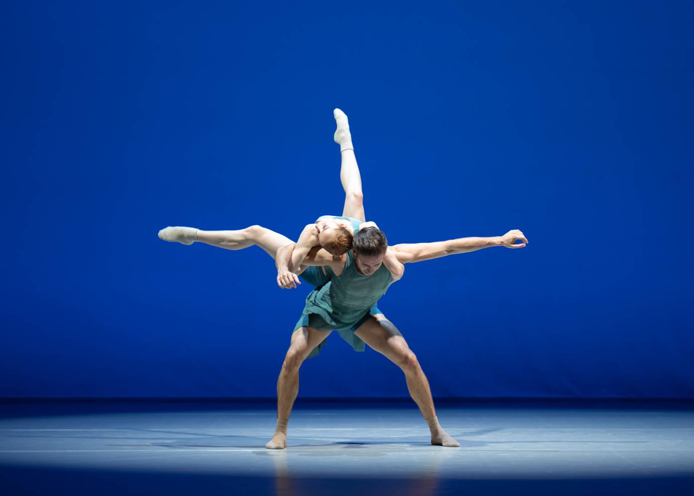 2 dancers in blue, one balancing on the back of the other in a lift