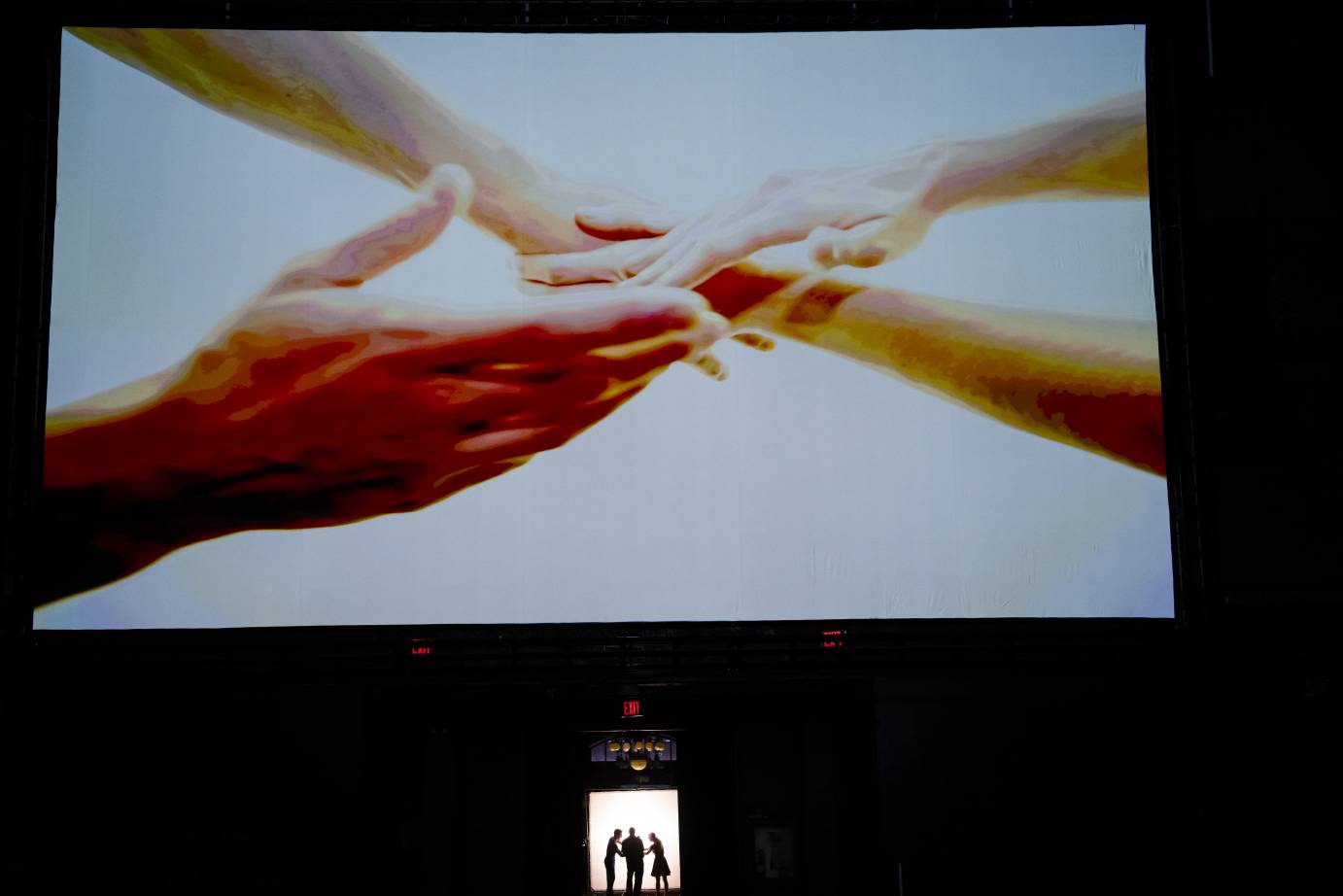 Giant-sized arms and hands are screened while those being screened are standing in a small room below.