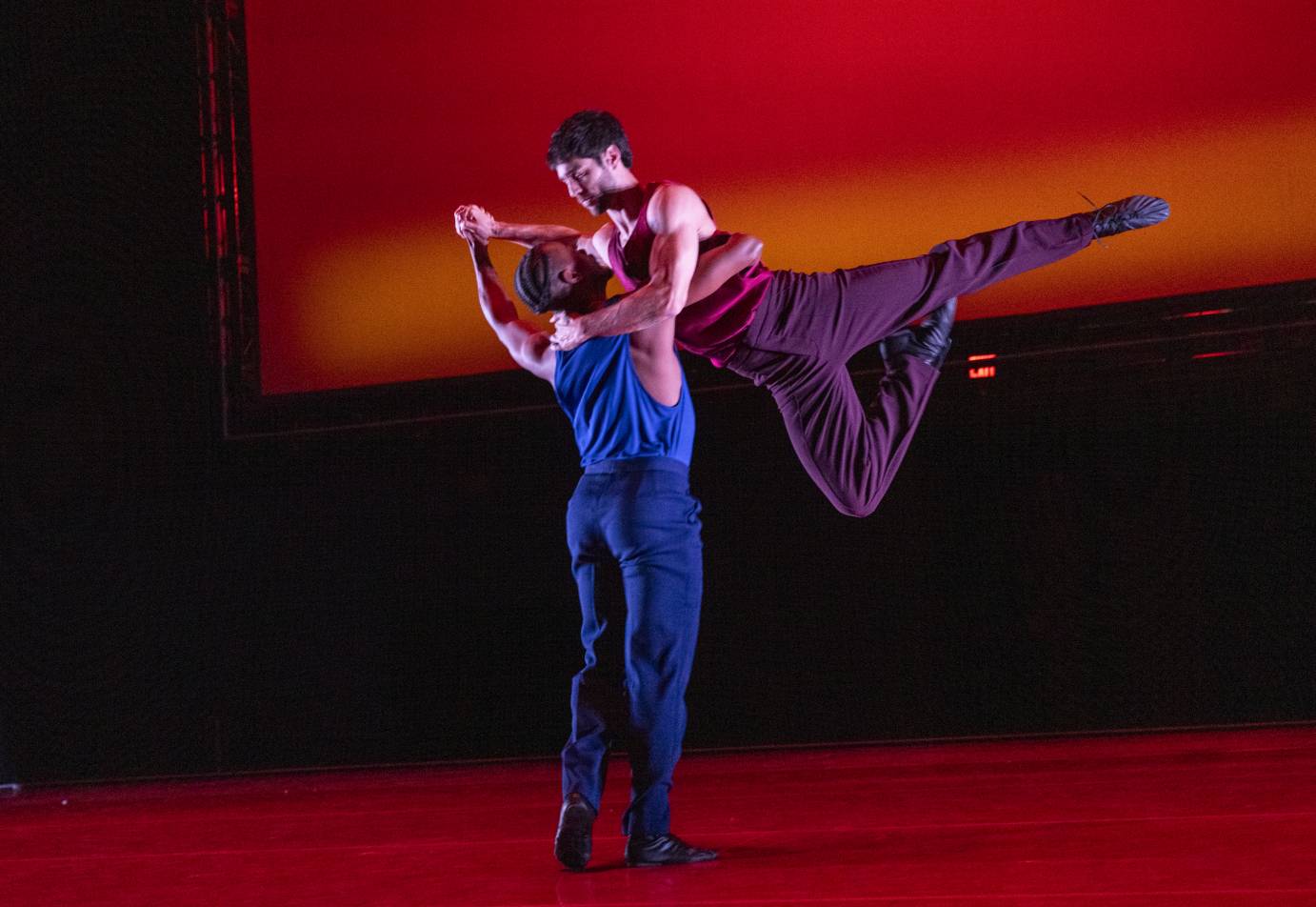 One man lifts another, the lifted one with one leg extended and the other in passe.