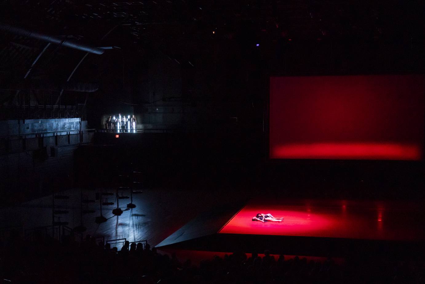 A view of the dead lovers in a pool of red light as stick bearers watch from a balcony high in the Armory