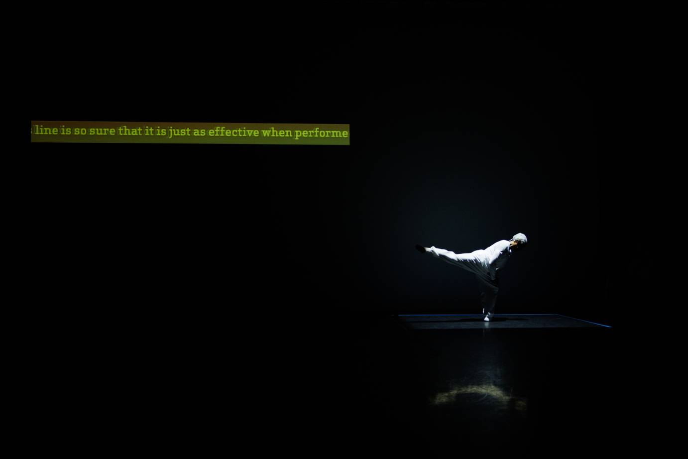 A far-away view of the white-haired, white-costumed man in back attitude with snatched words, including 