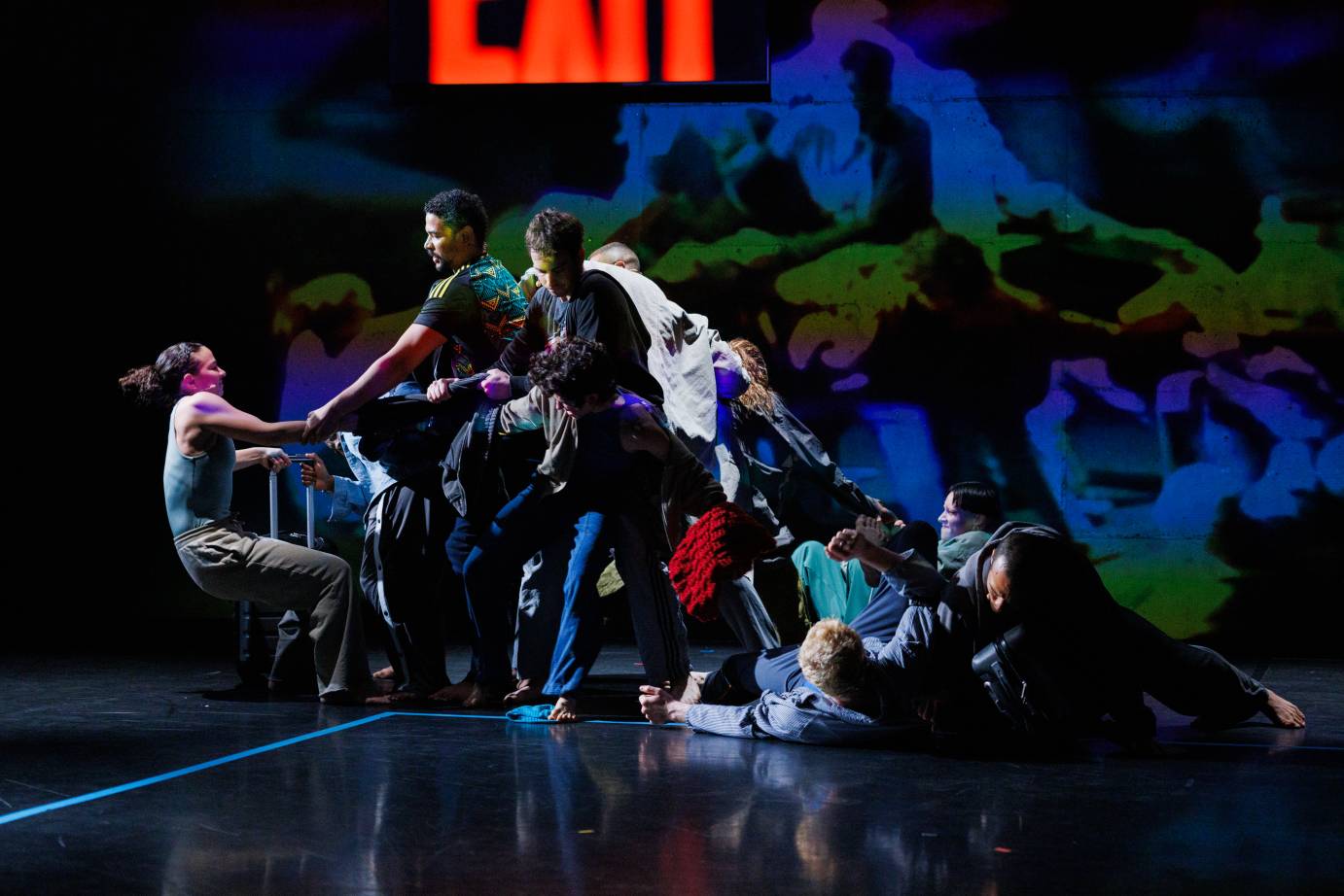 A group of dancers forming a 'triangle' from the floor to standing against a screened backdrop of green and blue.