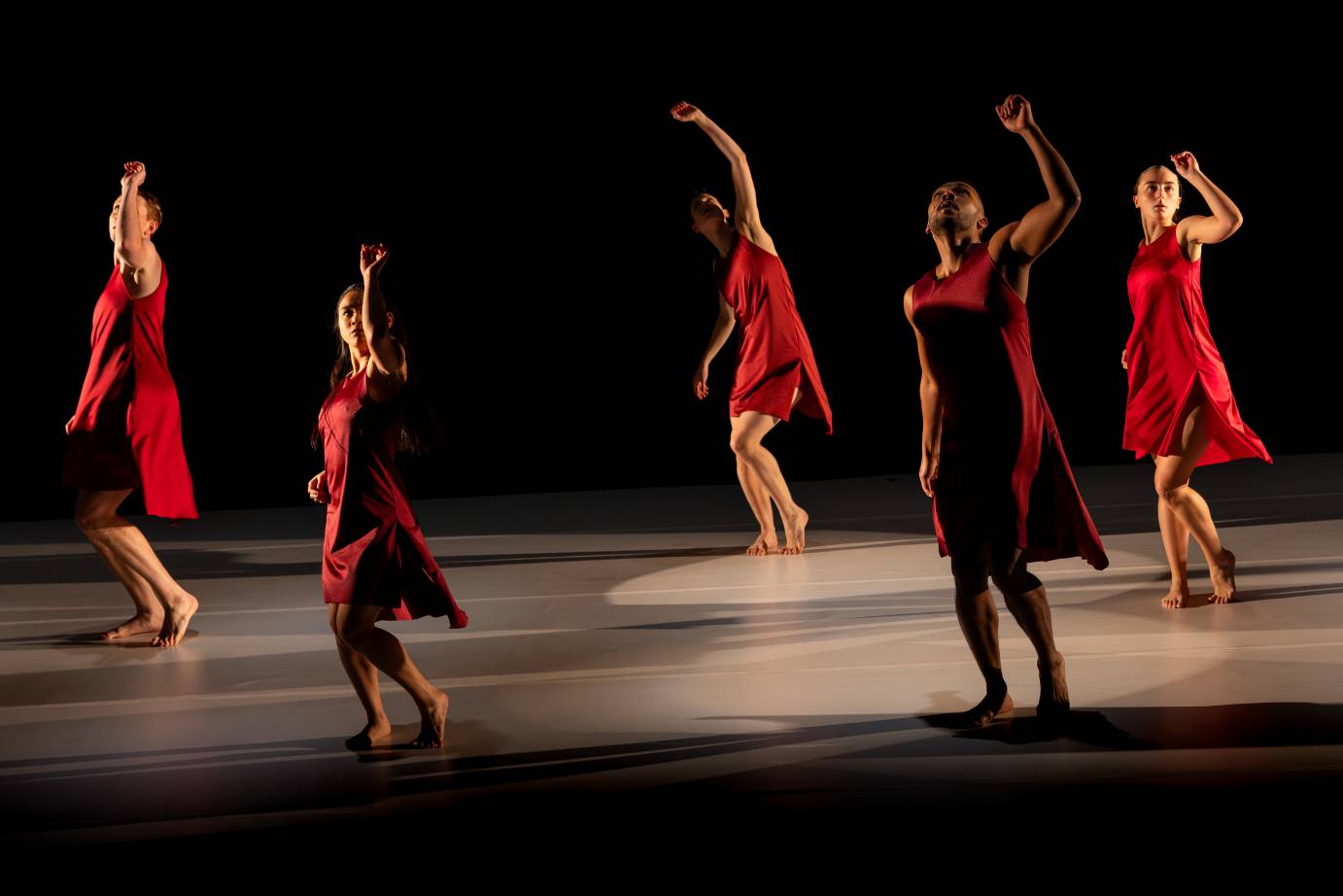 dancers in red dresses against a black background reach toward the sky