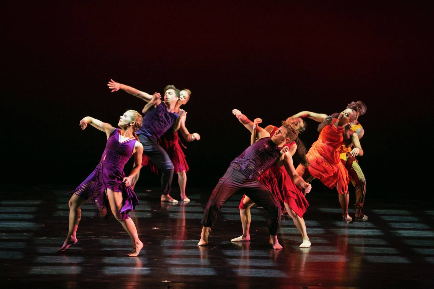 three couples and one solo dancer dressed in purples and shades of red extend their forearms to the side in reaction to someone of something