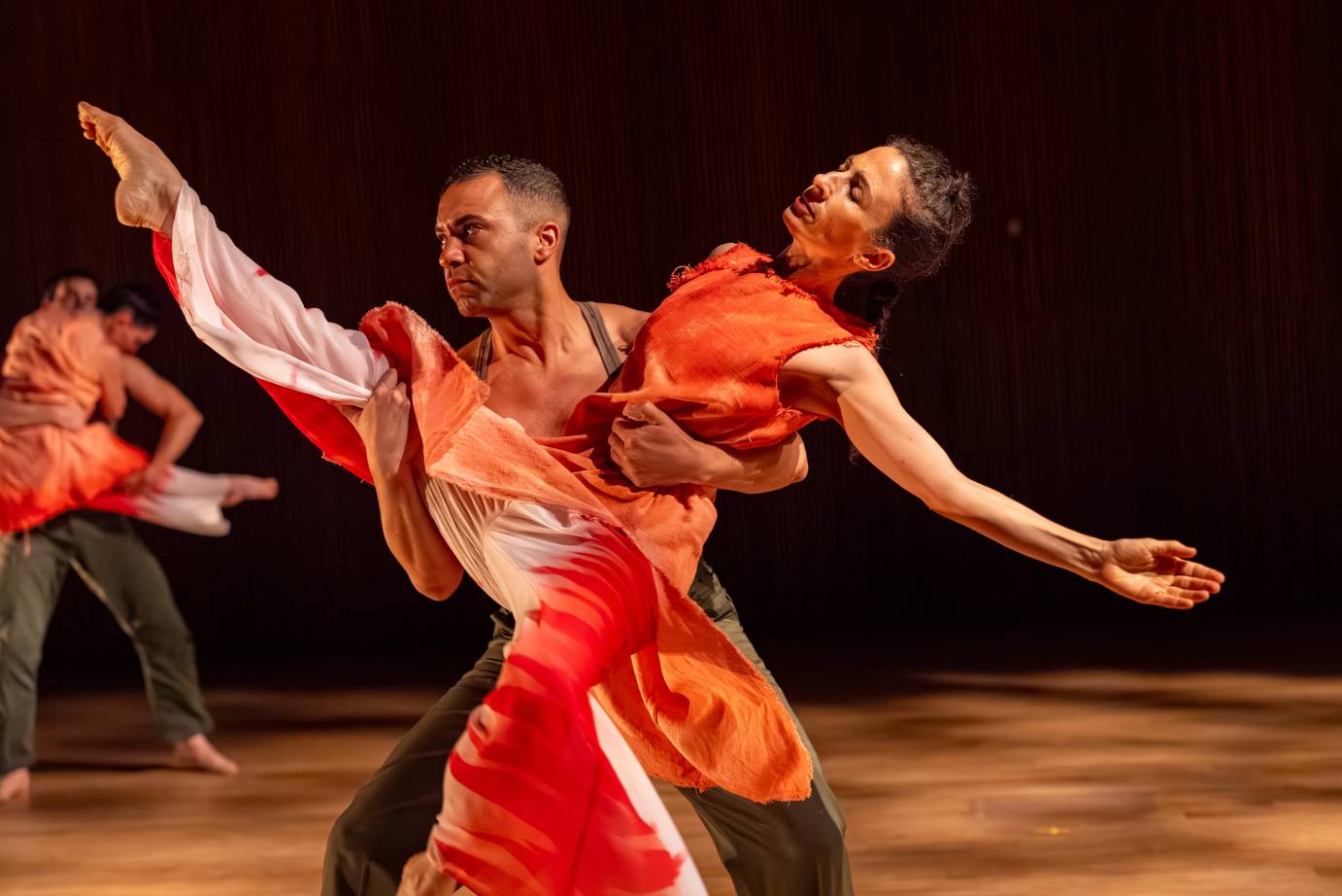 A woman on releve with her leg extended high on the diagonal leans back into a man's arms. Her eyes are closed as if she has succumbed to overwhelming feeling..