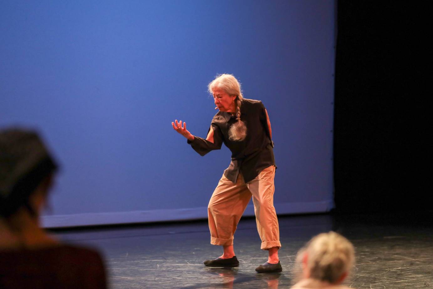An elderly woman with a long white braid looks into the palm of her hand as she slightly bends hip-width legs.
