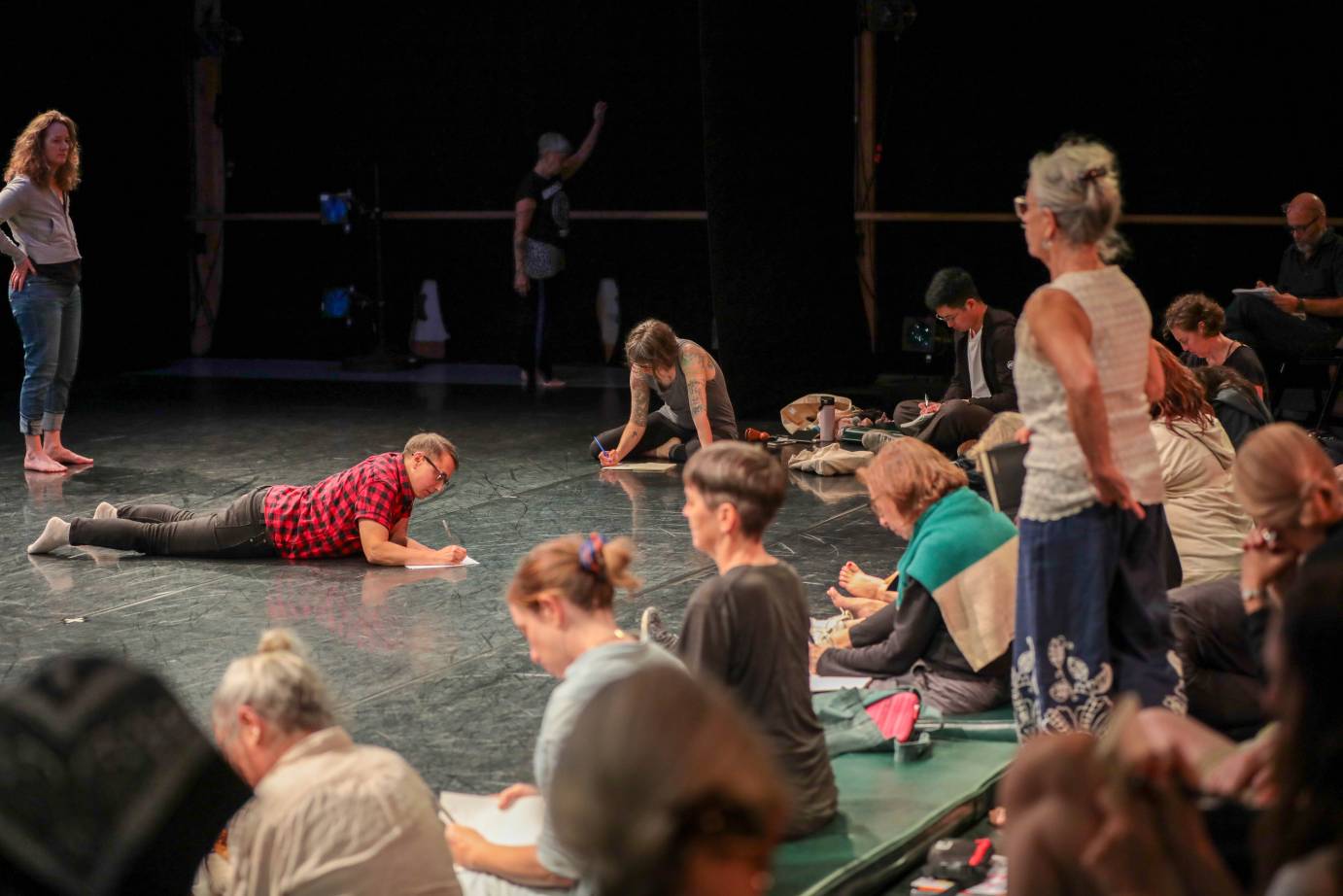 The audience, young and older, dressed casually in street clothes, lies and sit as they scribble in notebooks.