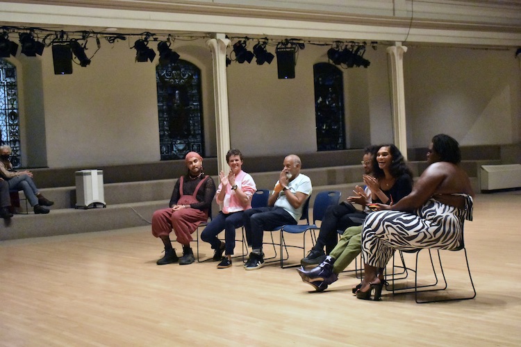 artists in street clothes sitting on blue chairs in the St. Marks Church space... everyone seems caught in a moment of joyous clapping 