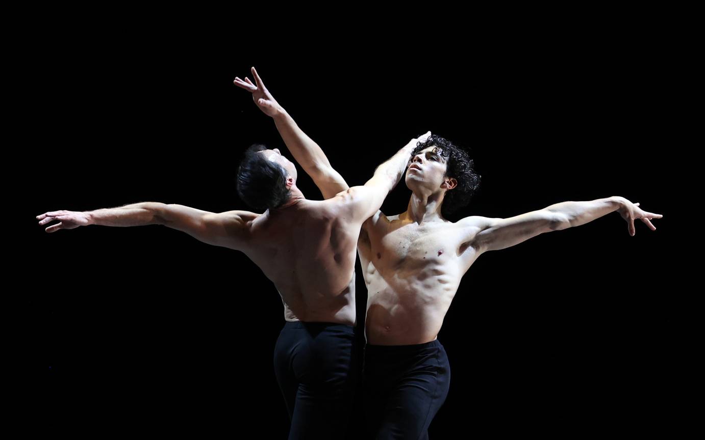 A male duet, chests bared, face one another lifting faces and arms upward.