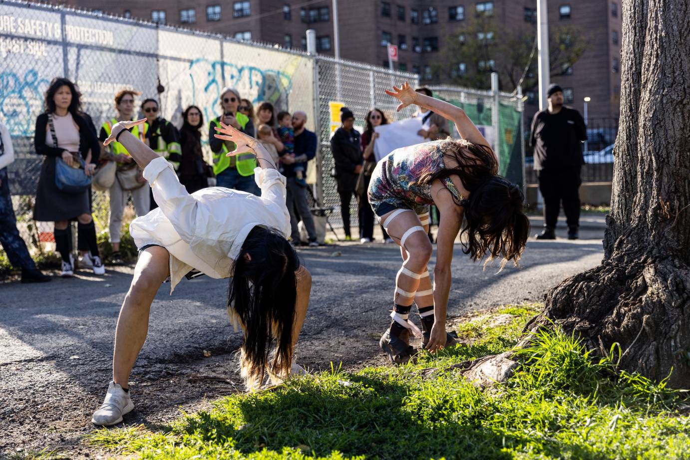 two women bend forward backs to audience. They are outside in the day light.