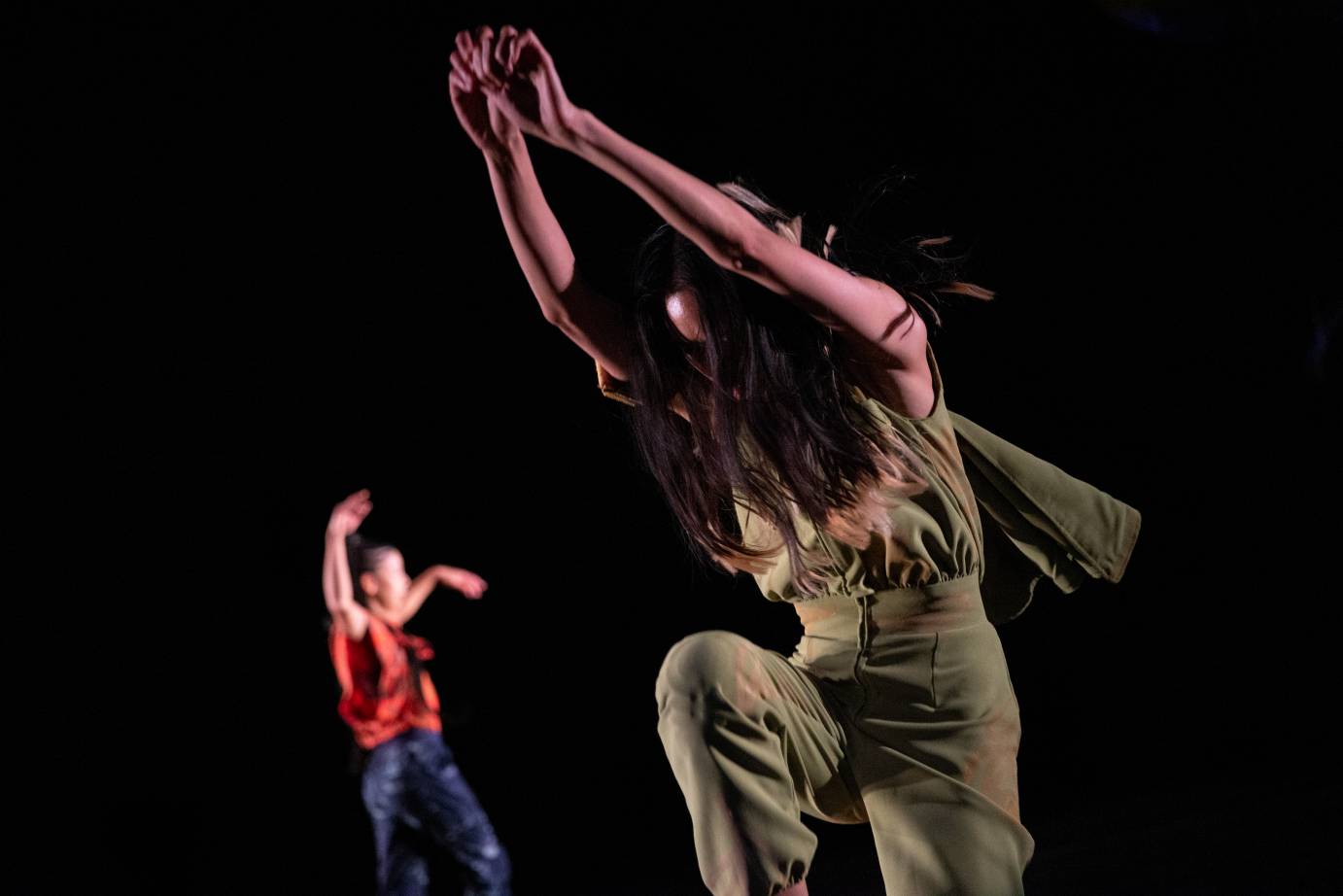 a woman in green leaps forward arms stretched upwards