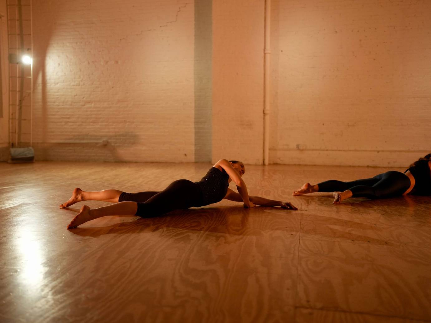 Two performers on their bellies on a rich bronze-colored floor.