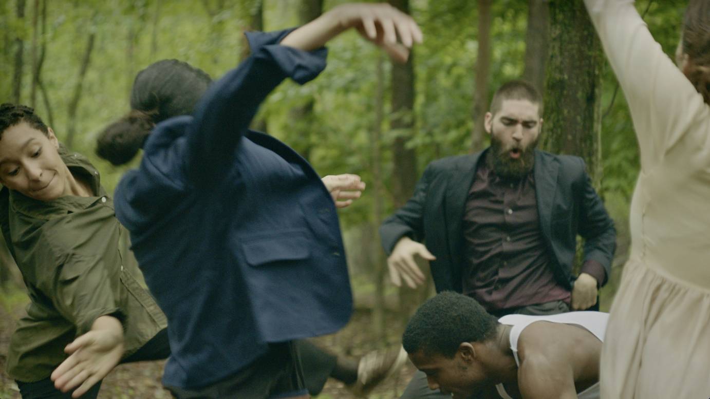 A group of body writhes as, center, a black man folds over. On the right side, a white man makes an OH sound