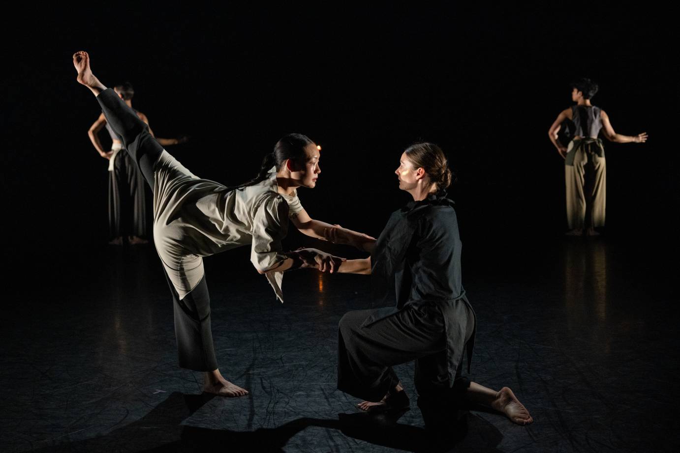 on a dimly lit stage dancer in tunics and lose pants pose...the mani figure in a arabesque holding hands with a crouching woman who supports her