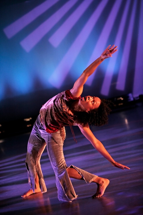 Gesel in a red velour shirt and pants looks at her hands as she bends to one side