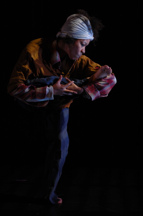 Gesel wears a headscarf. She holds one of her legs close to her chest while balancing on her other leg.