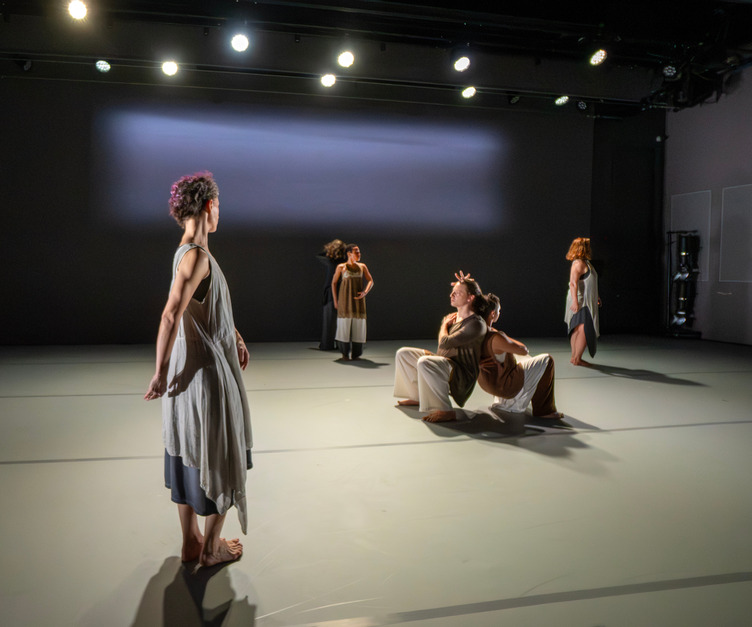A back-to-back duet in deep squats are surrounded by three standing dancers.