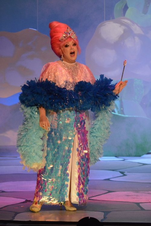 Dirty Martini wears a sequined evening gown and orange beehive wig while she sings.