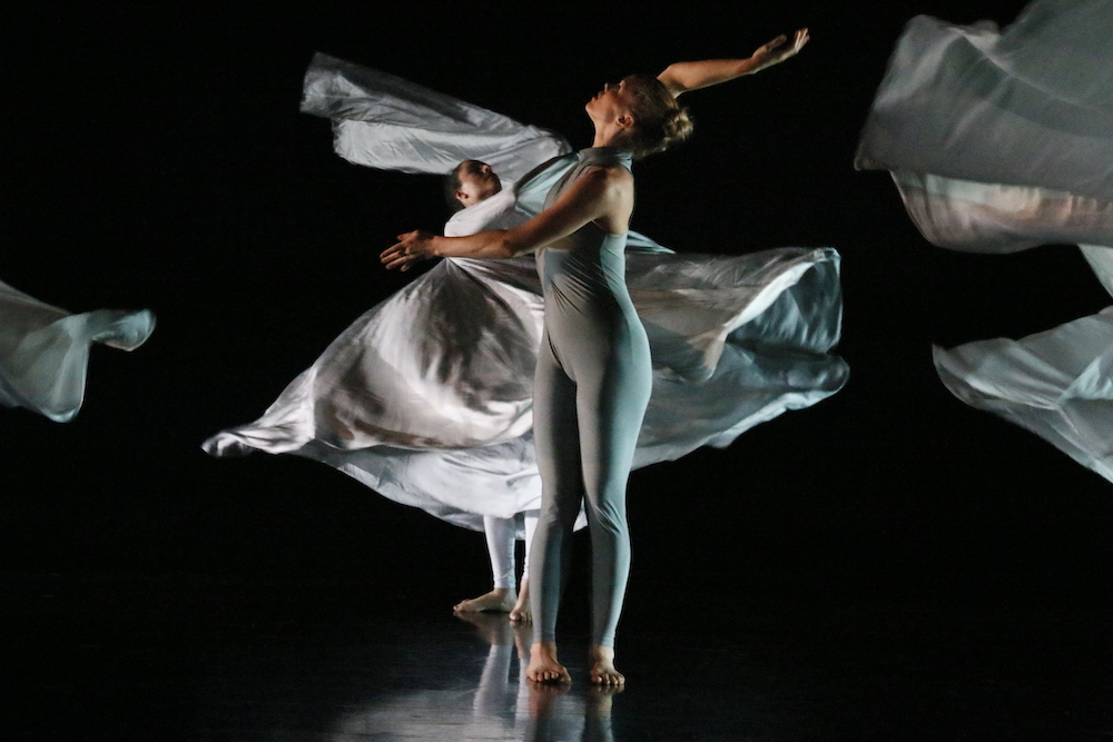 Jody Sperling in ice blue unitard swaying in front of women with Loie Fuller fabric costumes floating behind her 