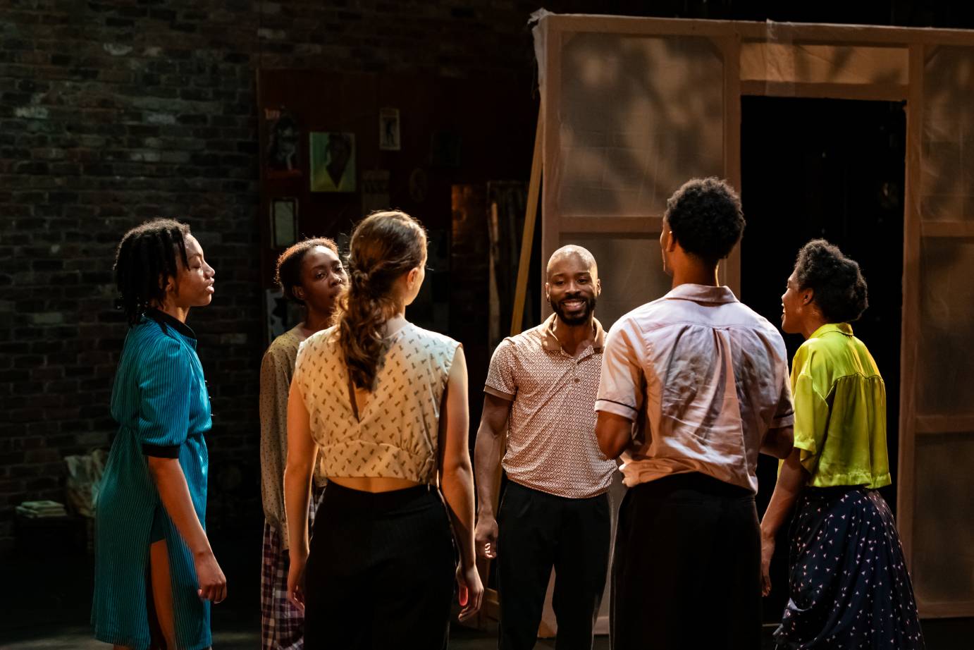 Six dancers stand in a circle facing one another with smiles on their lips