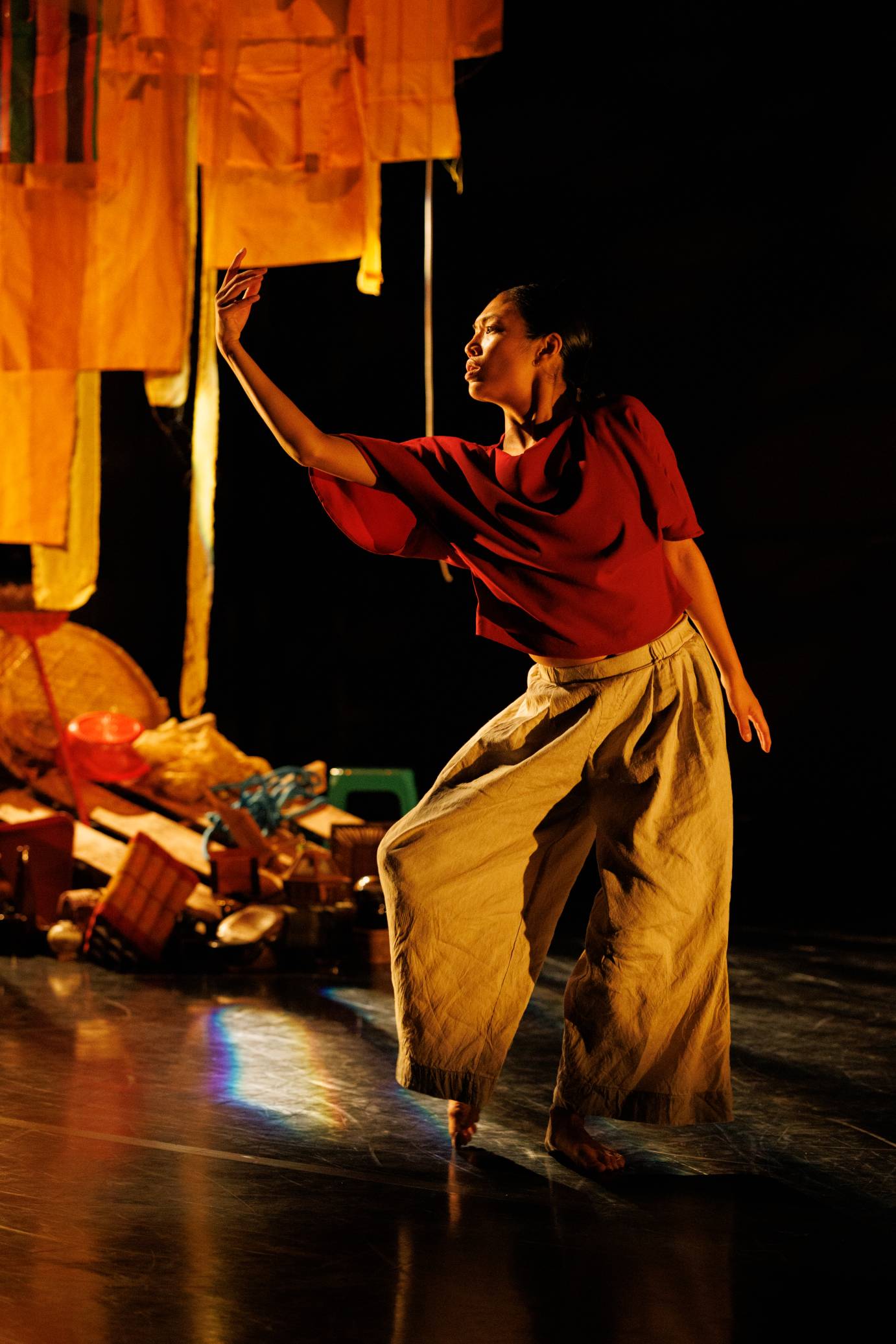A woman in a red shirt tilts her body toward numerous pieces of orange-lit cloth. Her soft fingers seemingly caress a lower edge.
