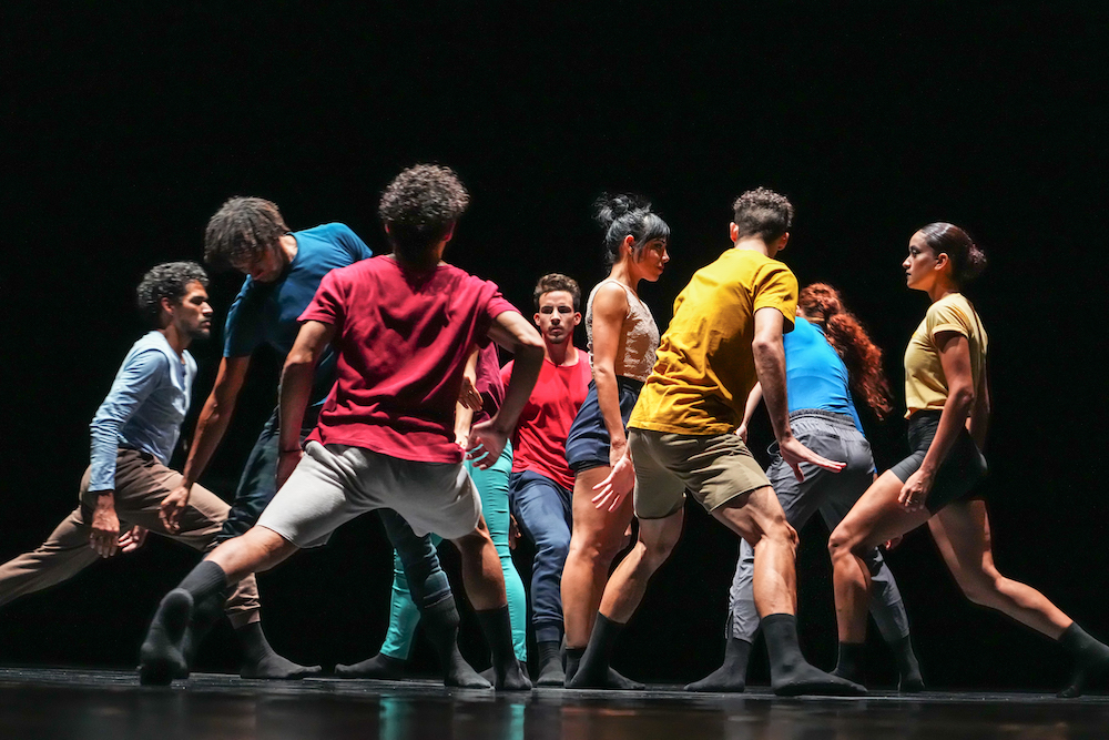 the group in colorful combinations of relaxed tshirts, tank tops, shorts, and tight leggings clump together in various positions creating an imperfect circle 