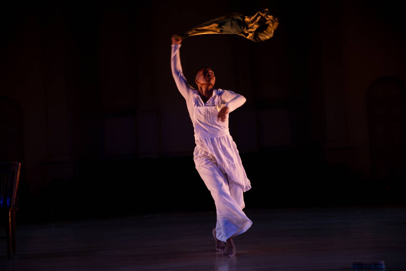 A woman dressed in white whips a gold cloth overhead.