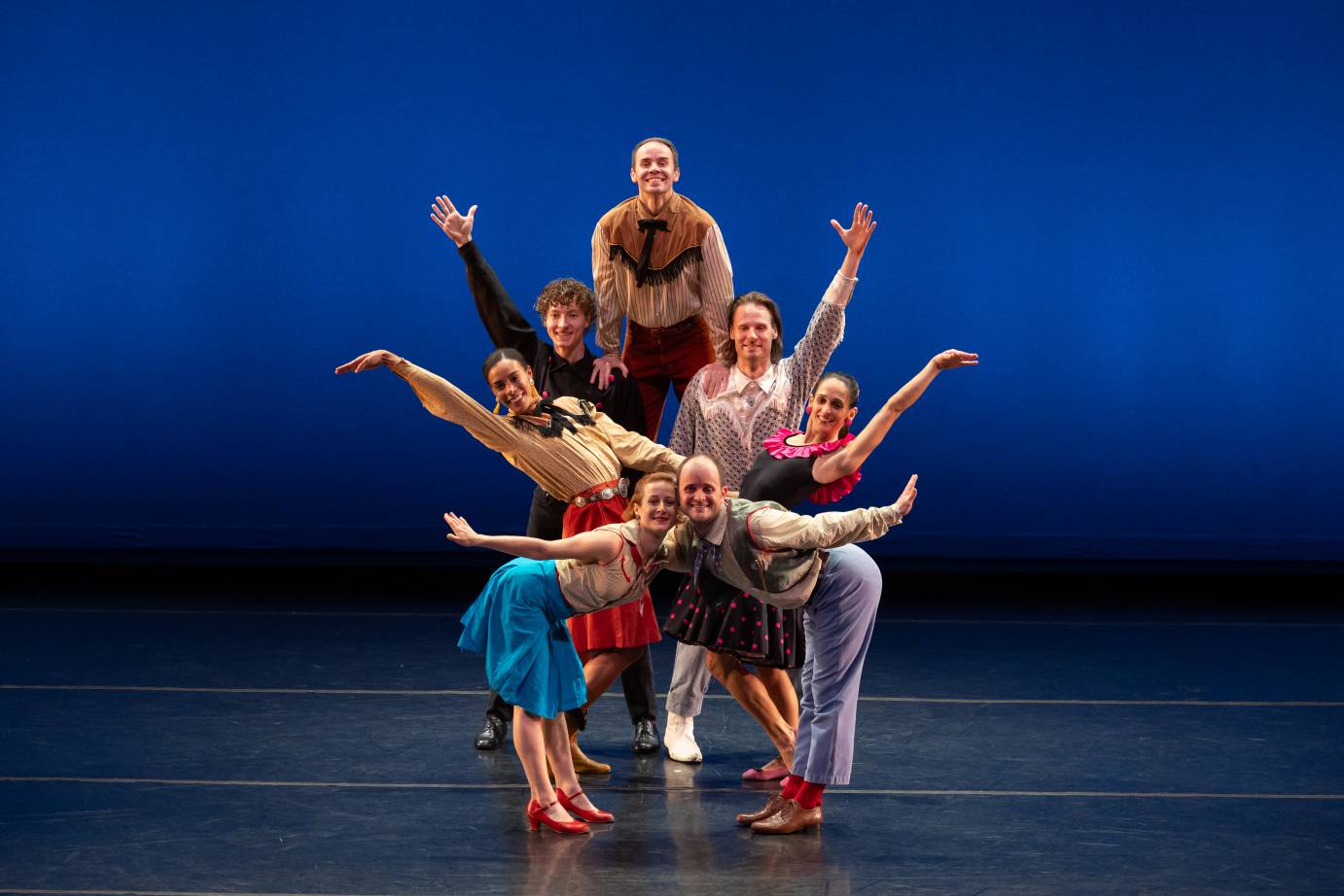 A group dressed in Western wear form a group 'howdy' by gathering together some dancers lifted by others arms raised
