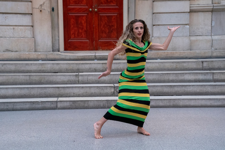 woman with curly brown blondish hair wearing a striped sheat juts her hip out and holds her arms in complementary angles