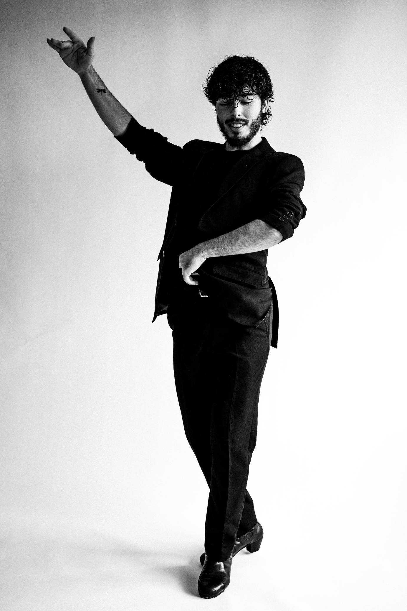 A dark-haired and bearded smiling man looks down as he manipulates castenets.