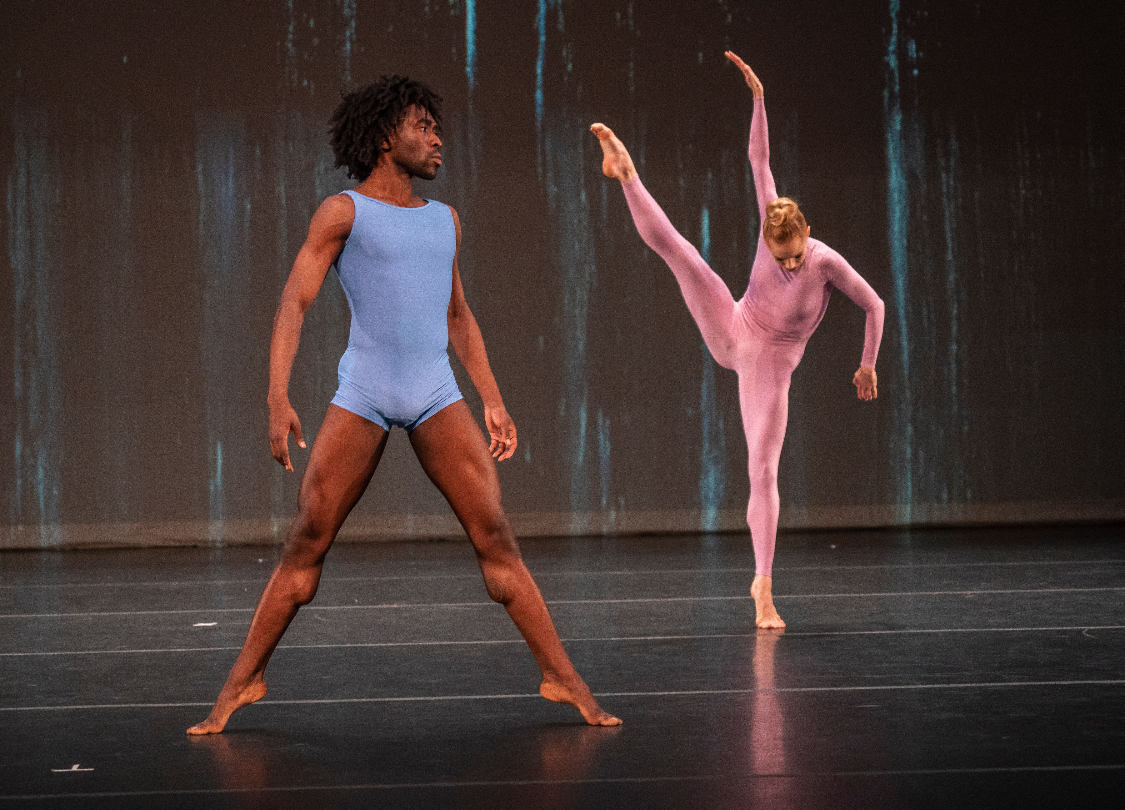 A man stands in second position while a woman extends her leg looking down